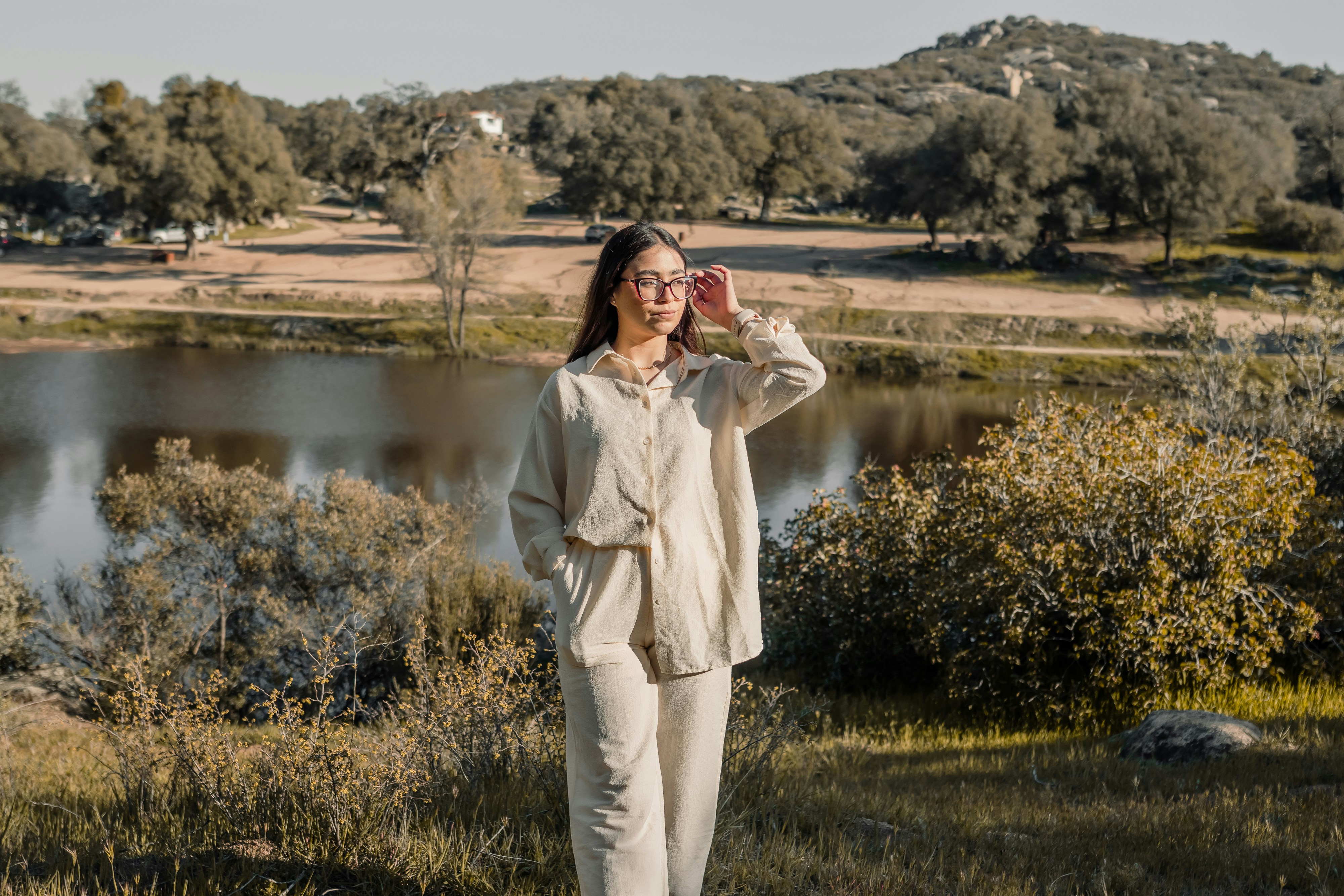 a woman standing in a field next to a lake