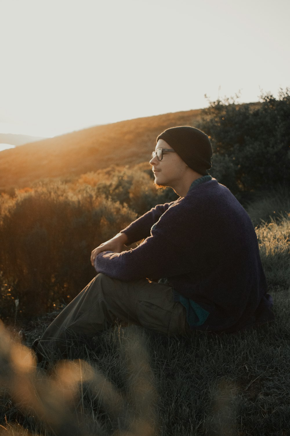 a man sitting in the grass with the sun behind him