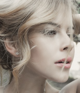 A close-up profile of a person with light hair elegantly styled. The image highlights soft facial features and natural makeup, creating an artistic and serene portrait.