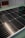 A close-up view of a solar panel with rows of rectangular photovoltaic cells. The surface appears glossy and reflective, indicating a clean and new condition. The background is slightly blurred, focusing attention on the panel's details.