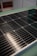 A close-up view of a solar panel with rows of rectangular photovoltaic cells. The surface appears glossy and reflective, indicating a clean and new condition. The background is slightly blurred, focusing attention on the panel's details.