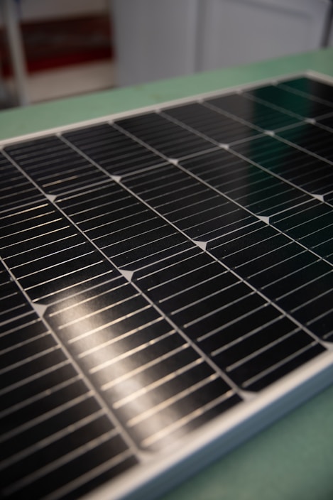 A close-up view of a solar panel with rows of rectangular photovoltaic cells. The surface appears glossy and reflective, indicating a clean and new condition. The background is slightly blurred, focusing attention on the panel's details.