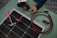 A collection of tools and materials on a flat surface, including a solar panel, a hammer with a pink handle, a multi-tool labeled 'Kobalt', an insulated screwdriver, and a pair of cables with connectors. A hand holds a wire cutter near several rolls of electrical tape.