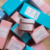 Multiple skincare product boxes and containers with labels featuring Skintific, including a jar labeled MSH Niacinamide Brightening Moisture Gel. The boxes are predominantly pastel blue and pink.