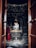 A dimly lit temple room containing a large, decorated lingam at the center. A person dressed in traditional attire stands nearby, possibly engaged in religious activity. The lingam is adorned with garlands and inscriptions, with small decorative items placed around it. Wooden doors frame the entrance to the room.