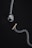 A silver chain with a prominent pendant at one end shaped like a detailed dog head and a small gold bone-shaped toggle clasp on a dark background. The overall composition is minimalistic and artistic, highlighting the metallic textures and intricate designs of the jewelry piece.