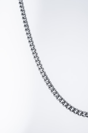 A close-up of a polished, metallic chain against a plain, light background. The chain appears to be made of interlocking loops that form a pattern.