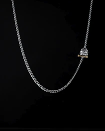 Close-up of a delicate silver necklace with a heart-shaped pendant holding a tiny photo inside, softly lit against a white background.
