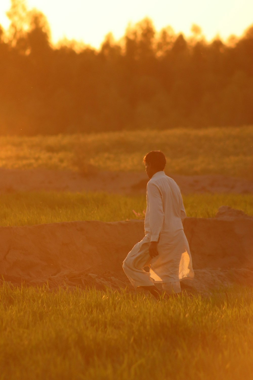 a man walking through a field at sunset