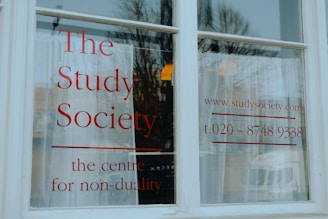 A white window with large, bold red lettering displaying 'The Study Society, the centre for non-duality', along with a web address and phone number.