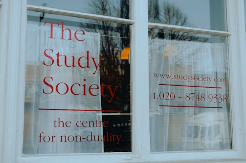 A white window with large, bold red lettering displaying 'The Study Society, the centre for non-duality', along with a web address and phone number.