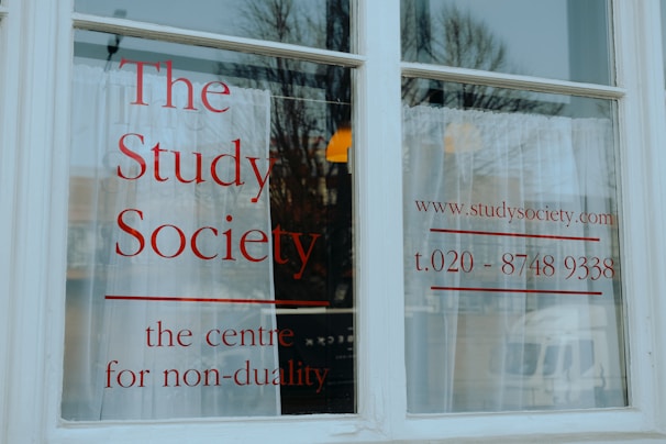A white window with large, bold red lettering displaying 'The Study Society, the centre for non-duality', along with a web address and phone number.