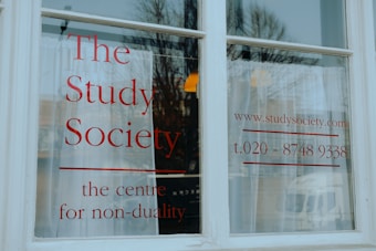 A white window with large, bold red lettering displaying 'The Study Society, the centre for non-duality', along with a web address and phone number.
