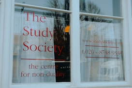 A white window with large, bold red lettering displaying 'The Study Society, the centre for non-duality', along with a web address and phone number.