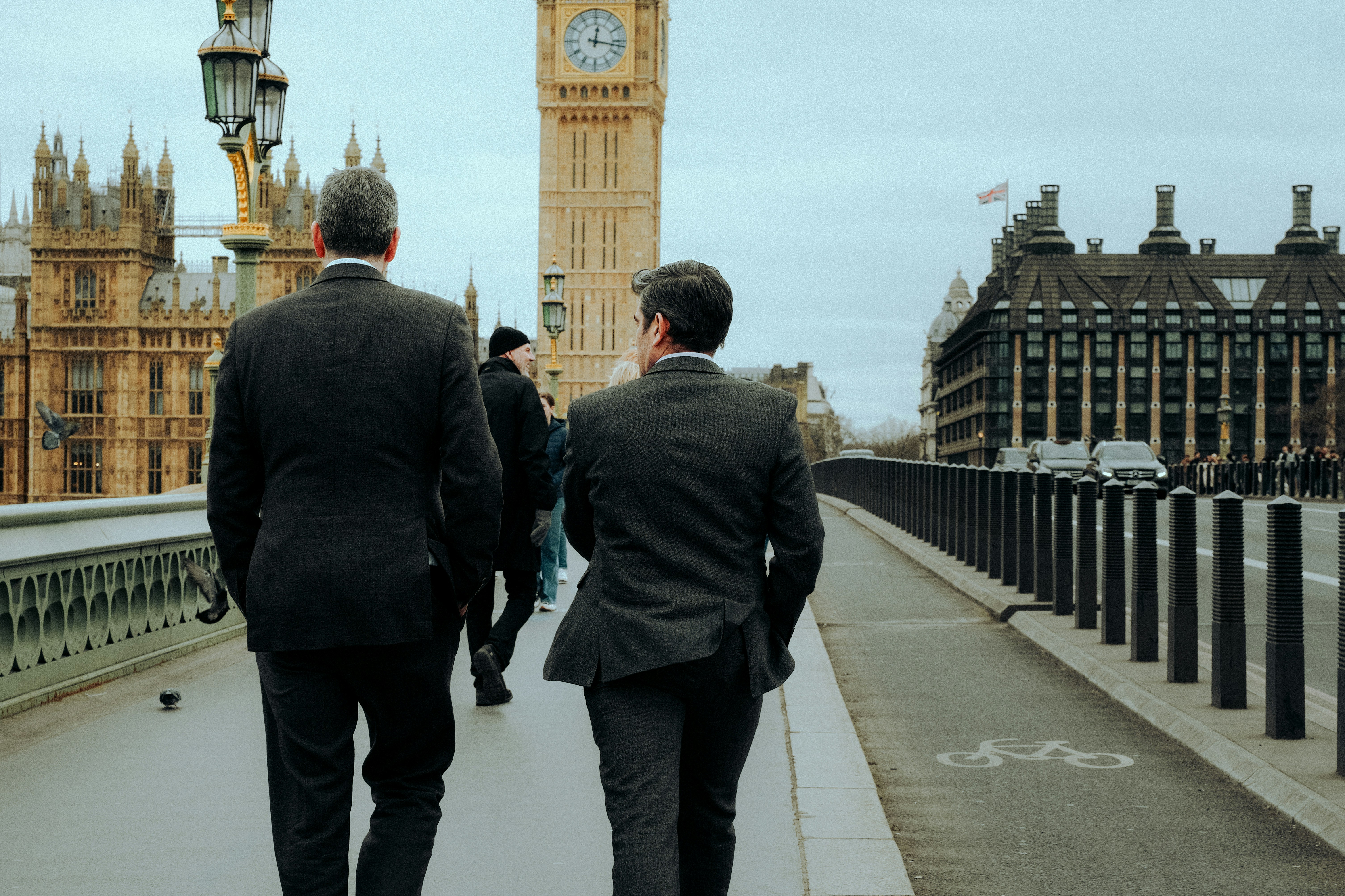 two men in suits walking across a bridge