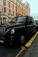 A sleek black taxi waiting at a sunny Leyton street corner.
