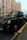 A classic black taxi is parked on the side of a street with a red brick building in the background. The taxi has a distinct shape and design typical of British cabs and is positioned next to a yellow line.