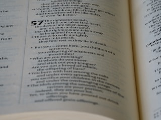 A close-up view of an open book displaying text with multiple paragraphs. The text appears to be poetry or scripture with numbers indicating different sections. The page has a cream-colored background with black typography.