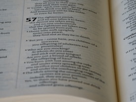 A close-up view of an open book displaying text with multiple paragraphs. The text appears to be poetry or scripture with numbers indicating different sections. The page has a cream-colored background with black typography.