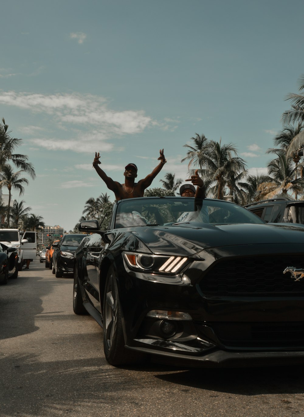 two men waving from the top of a black car