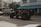 A black Jeep with open doors and red interior is parked on the street in front of a building labeled 'Shore Park Hotel'. Nearby, a van with colorful graffiti-style text reading 'AZUCAR' serves as a backdrop, and there's a café entrance with a blue awning named 'Larios on the Beach'. The scene captures a relaxed, vibrant atmosphere with a mix of vehicles and pedestrians.