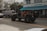 A black Jeep with open doors and red interior is parked on the street in front of a building labeled 'Shore Park Hotel'. Nearby, a van with colorful graffiti-style text reading 'AZUCAR' serves as a backdrop, and there's a café entrance with a blue awning named 'Larios on the Beach'. The scene captures a relaxed, vibrant atmosphere with a mix of vehicles and pedestrians.
