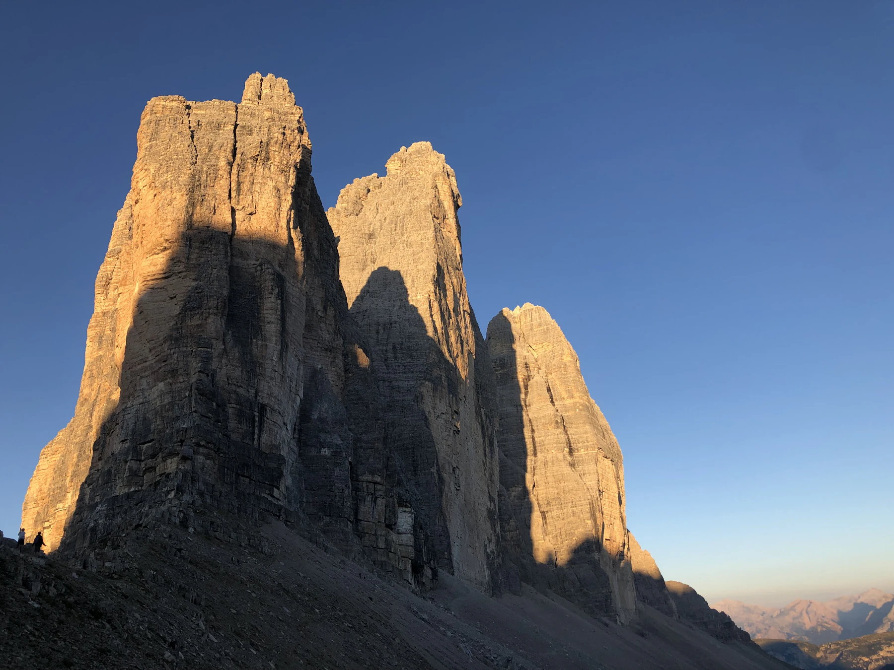 Photograph of Tre Cime di Lavaredo catching warm early light above a pale mountain ridge.