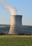 a power plant emits smoke as it sits in the middle of a field