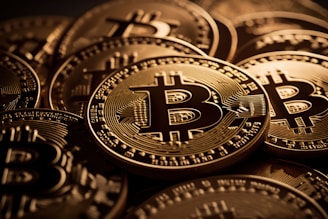A close-up view of multiple shiny gold coins featuring the Bitcoin logo with intricate circuit-like patterns. The coins are stacked and overlap each other, creating a sense of abundance and wealth.