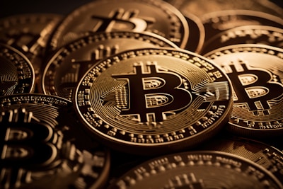A close-up view of multiple shiny gold coins featuring the Bitcoin logo with intricate circuit-like patterns. The coins are stacked and overlap each other, creating a sense of abundance and wealth.