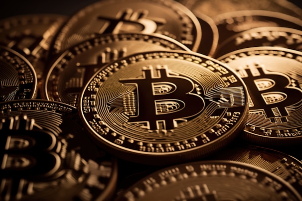 A close-up view of multiple shiny gold coins featuring the Bitcoin logo with intricate circuit-like patterns. The coins are stacked and overlap each other, creating a sense of abundance and wealth.