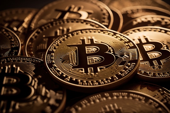 A close-up view of multiple shiny gold coins featuring the Bitcoin logo with intricate circuit-like patterns. The coins are stacked and overlap each other, creating a sense of abundance and wealth.