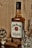 A bottle of Jim Beam Kentucky Straight Bourbon Whiskey is placed in the center. To the right, there is a crystal whiskey glass, and to the left, a cigar and a pocket watch are also visible. The setting has a warm and vintage atmosphere with a wooden background.