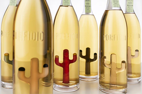 Elegant bottles of ultrapi lined up on a wooden table, with agave plants in the background.