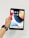 A hand holding a black tablet with a colorful home screen displaying various app icons. The person is wearing a black smartwatch. The background is plain and white.