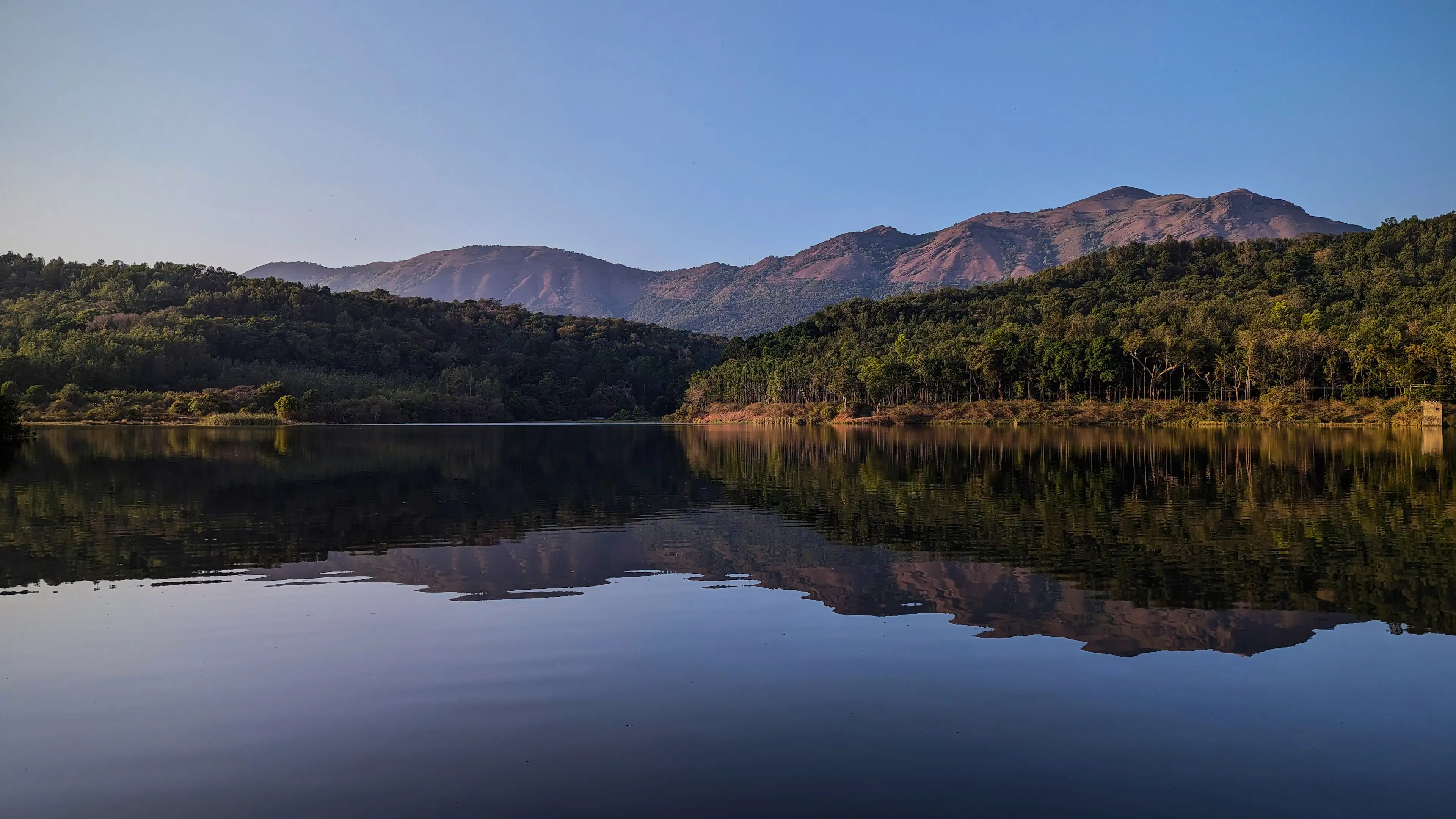 Still backwaters reflecting forested Ghats hills at dusk