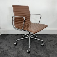 A modern office chair with a sleek design, featuring a brown padded seat and backrest made of leather or a similar material. The chair has metal armrests and a chrome-finished, five-point base with caster wheels, resting on a dark carpeted floor against a plain white wall.