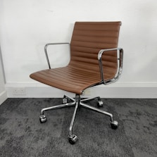 A modern office chair with a sleek design featuring brown cushioning and chrome armrests. It has a ribbed texture on the seat and backrest, set on a five-wheel base suitable for easy movement on carpet flooring. The chair is positioned against a plain white wall.