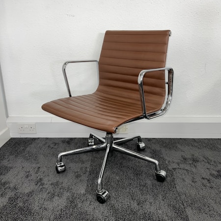 A modern office chair with a sleek design featuring brown cushioning and chrome armrests. It has a ribbed texture on the seat and backrest, set on a five-wheel base suitable for easy movement on carpet flooring. The chair is positioned against a plain white wall.