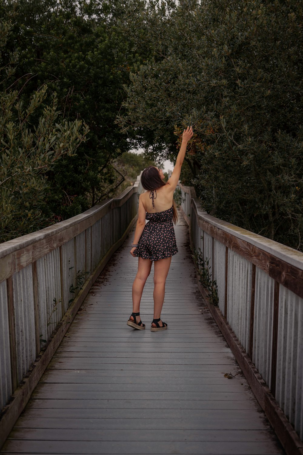 a woman standing on a bridge reaching up into the sky