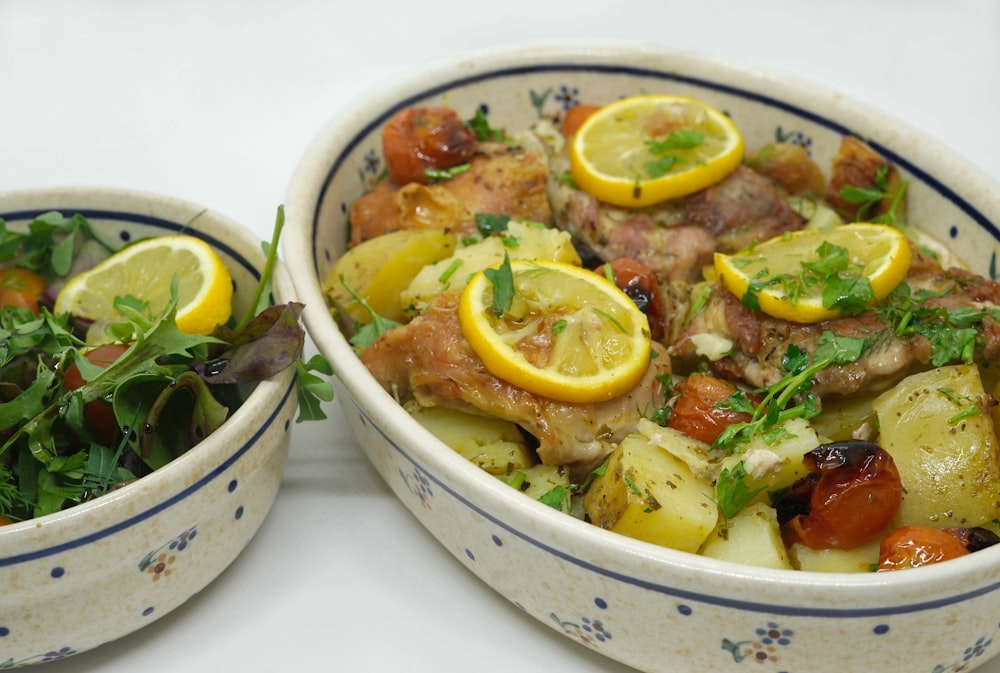 two bowls of food with lemons, meat, and vegetables