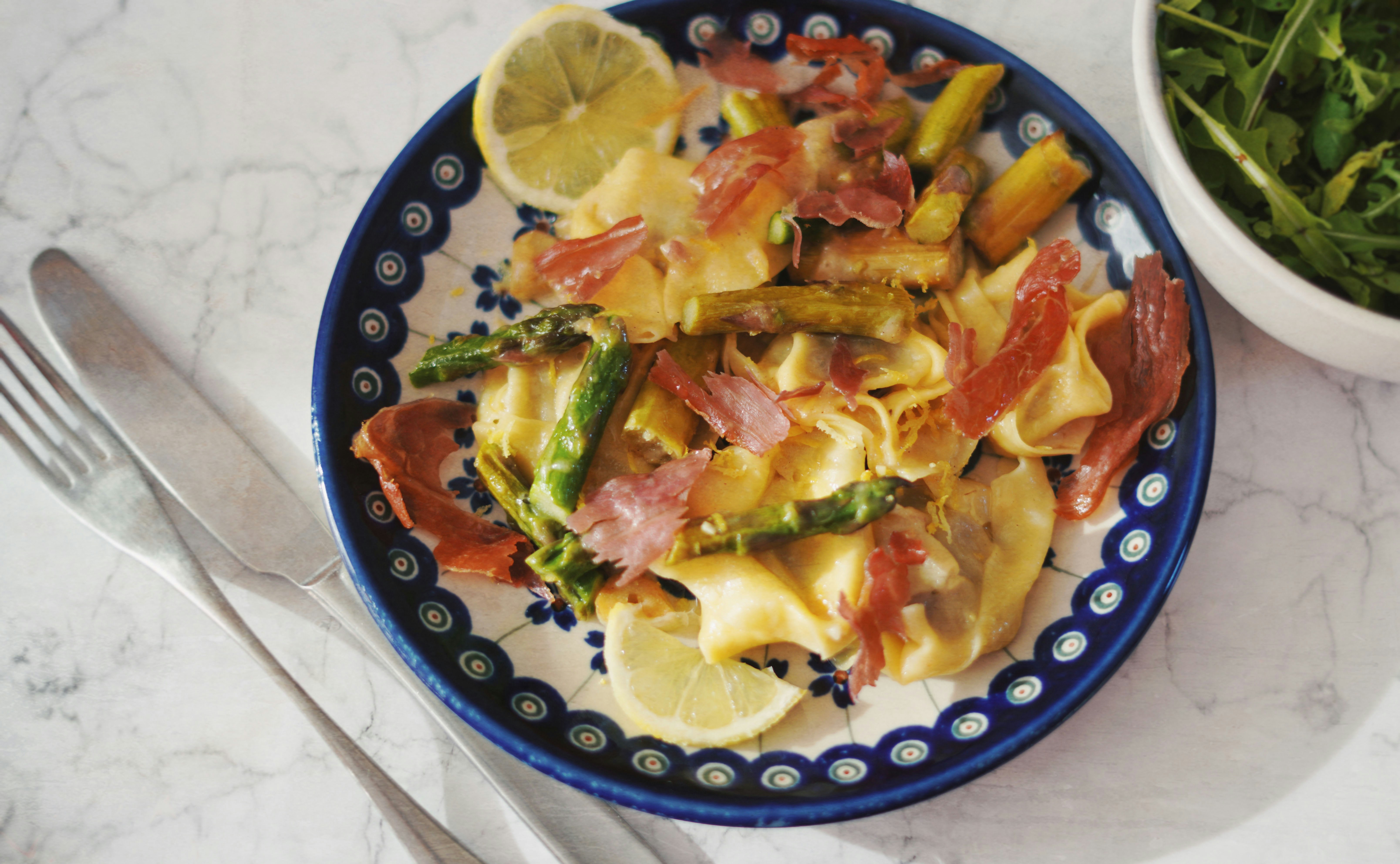 a blue and white plate topped with pasta and asparagus
