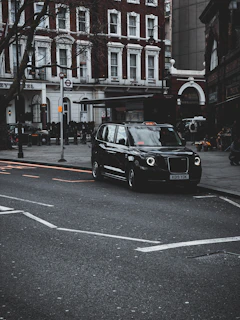A sleek black taxi parked outside a bustling London airport terminal at sunset