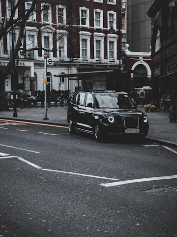 A sleek black taxi parked outside Winchester Cathedral on a sunny day, ready to pick up passengers.
