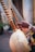 A close-up of a musical instrument featuring wooden pegs and strings, held by a person with a watch on their wrist. The body of the instrument is decorated with intricate patterns resembling musical symbols, crafted with beads. The setting appears to be an outdoor area with a blurred background.