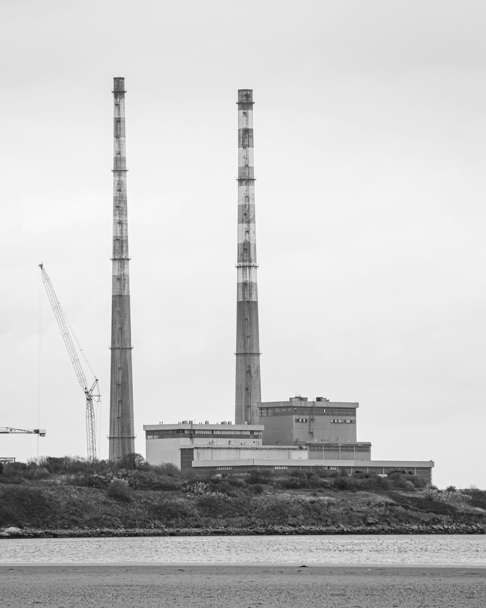 a black and white photo of a factory with cranes in the background