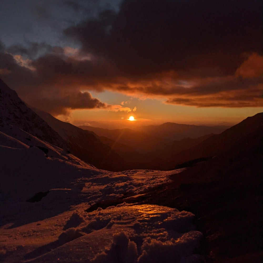 the sun is setting over a snowy mountain