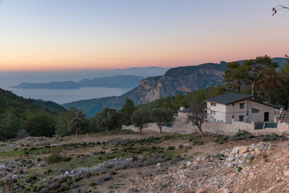 A serene Himalayan mountain view with a luxury farmhouse nestled among pine trees at sunset.