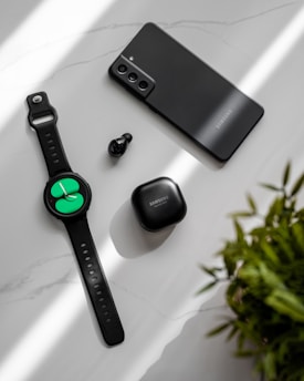 A flat lay arrangement of modern electronic devices, including a smartphone, smartwatch, wireless earbuds, and their charging case, all set against a minimalist marble-like surface. The lighting casts soft shadows, creating a sleek and contemporary aesthetic.