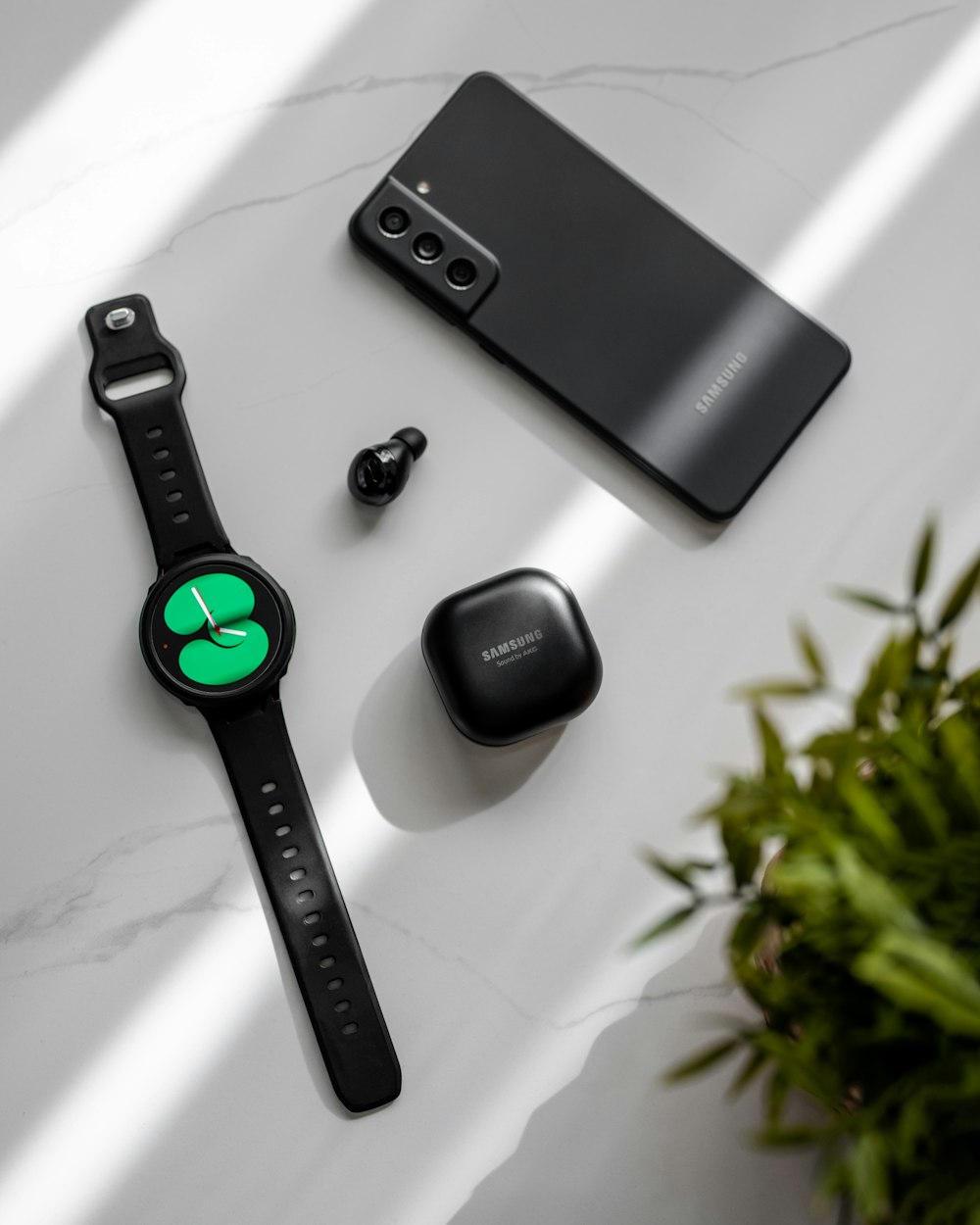 Eine Smartwatch, ein Handy und eine Pflanze auf einem Tisch